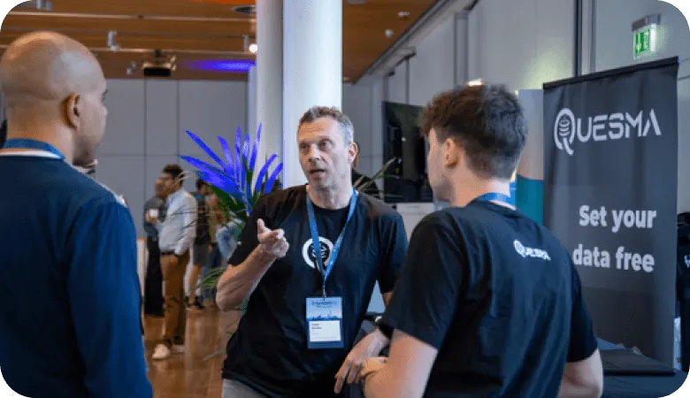 Three men talking at a tech event near a Quesma banner reading “Set your data free”