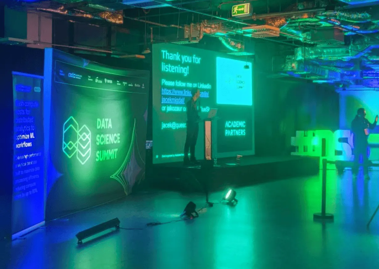 Speaker presenting on stage at Data Science Summit in Warsaw with slides projected behind.